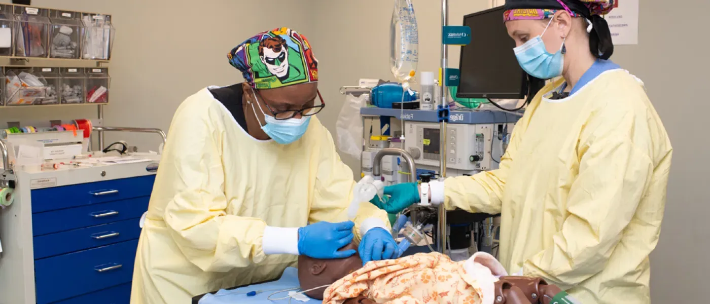 A U N E health professions student wearing scrubs works on a patient simulator